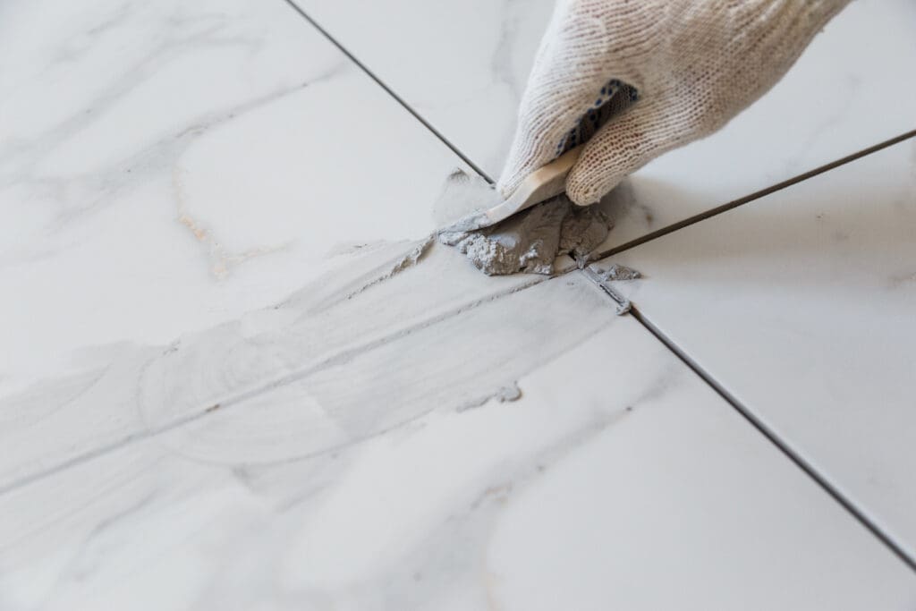 A close-up of a worker applying grout between marble tiles using a trowel, highlighting the process of tile and grout maintenance.